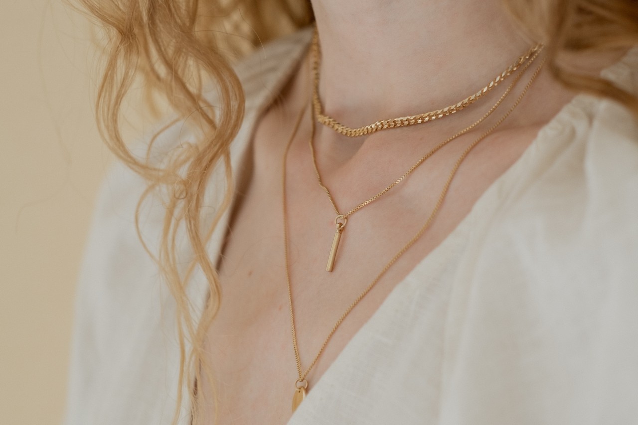 Woman wearing multiple gold necklaces along with a light colored shirt