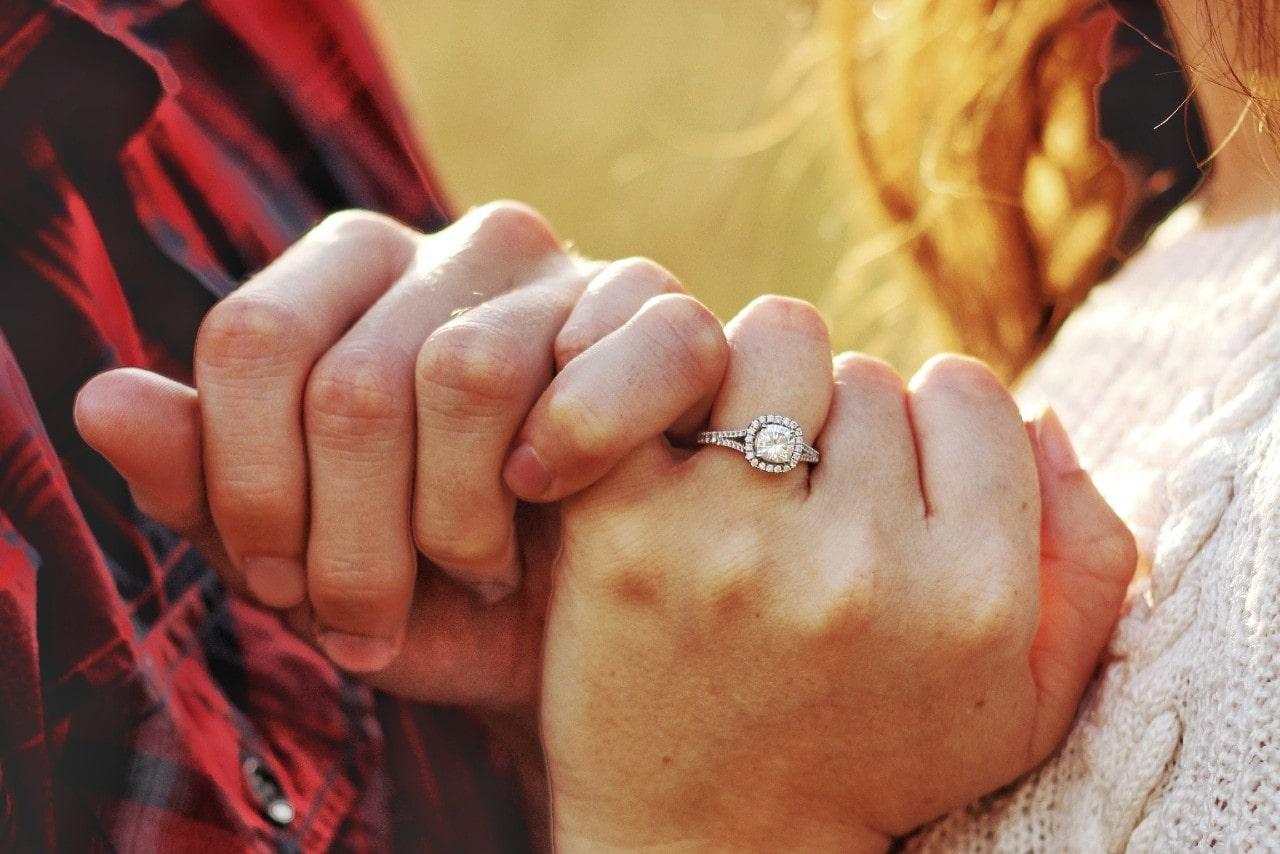 a couple intertwining pinkies, the woman wearing a halo engagement ring
