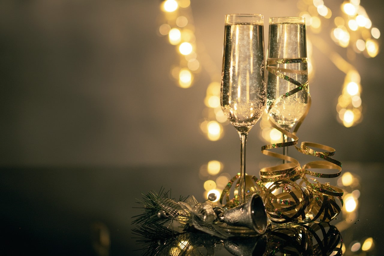 Two flute champagne glasses with gold ribbon and fairy lights in the background