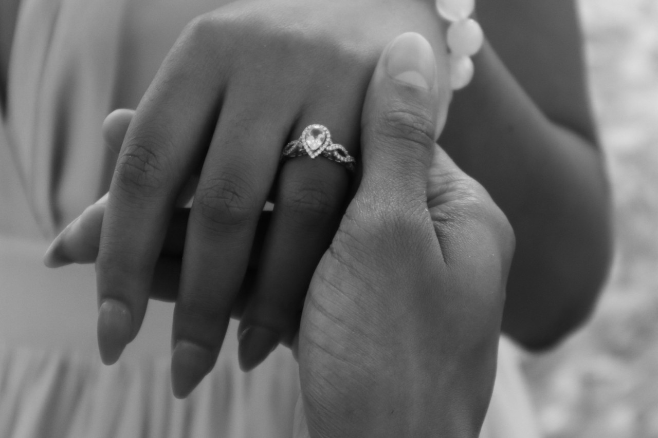 A pear shaped diamond halo engagement ring with an interweaving band on the hand of a woman being held by her love