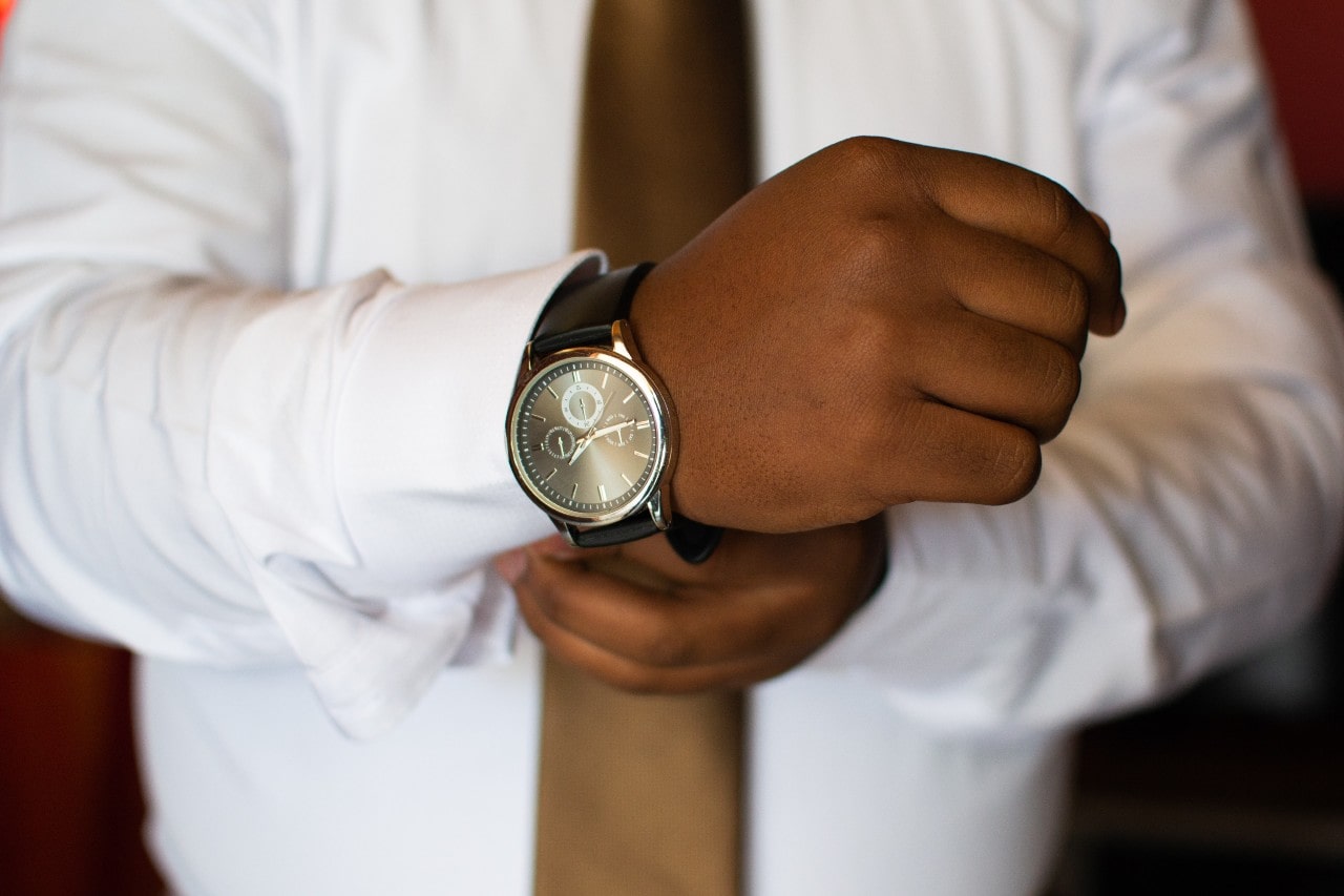 A man wearing a tie and button down shirt is putting on a high-end watch
