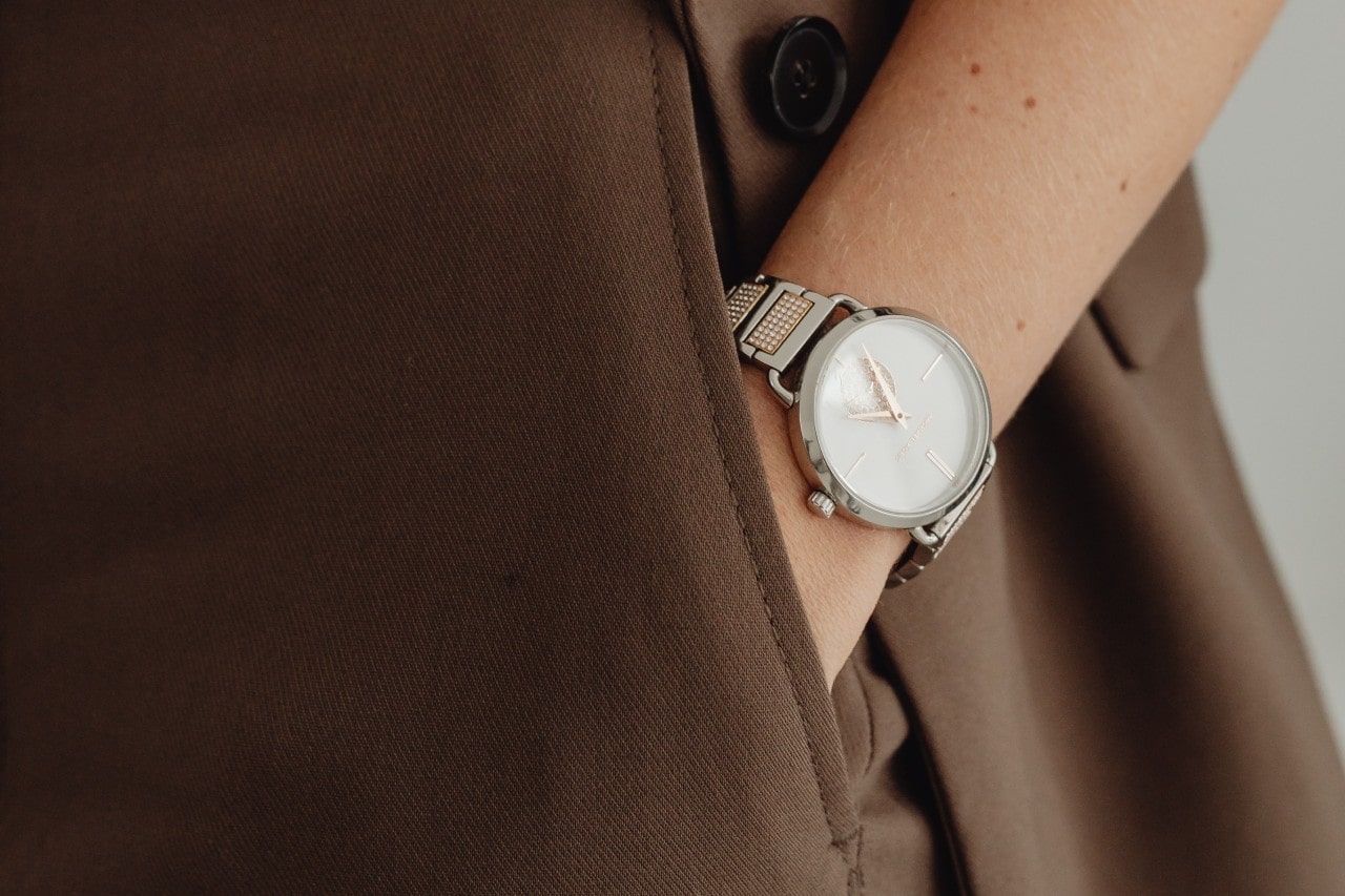 A woman wearing a multi-metal watch with diamond details shown on her wrist while her hand is in her pocket