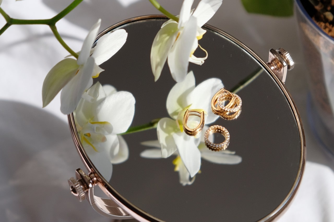 Gold and diamond fashion rings resting on a mirror surrounded by white orchids