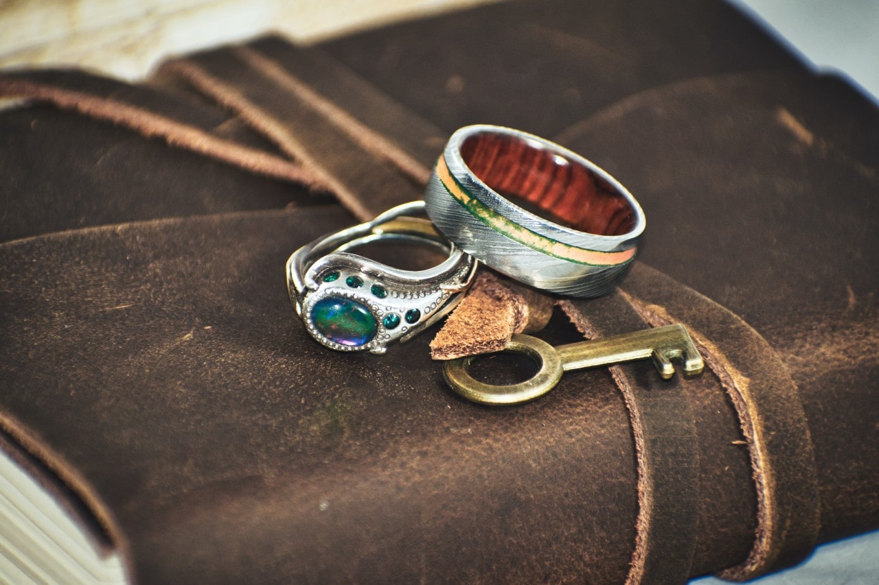 Wedding band and fashion ring with an assortment of objects resting on a leather-bound book