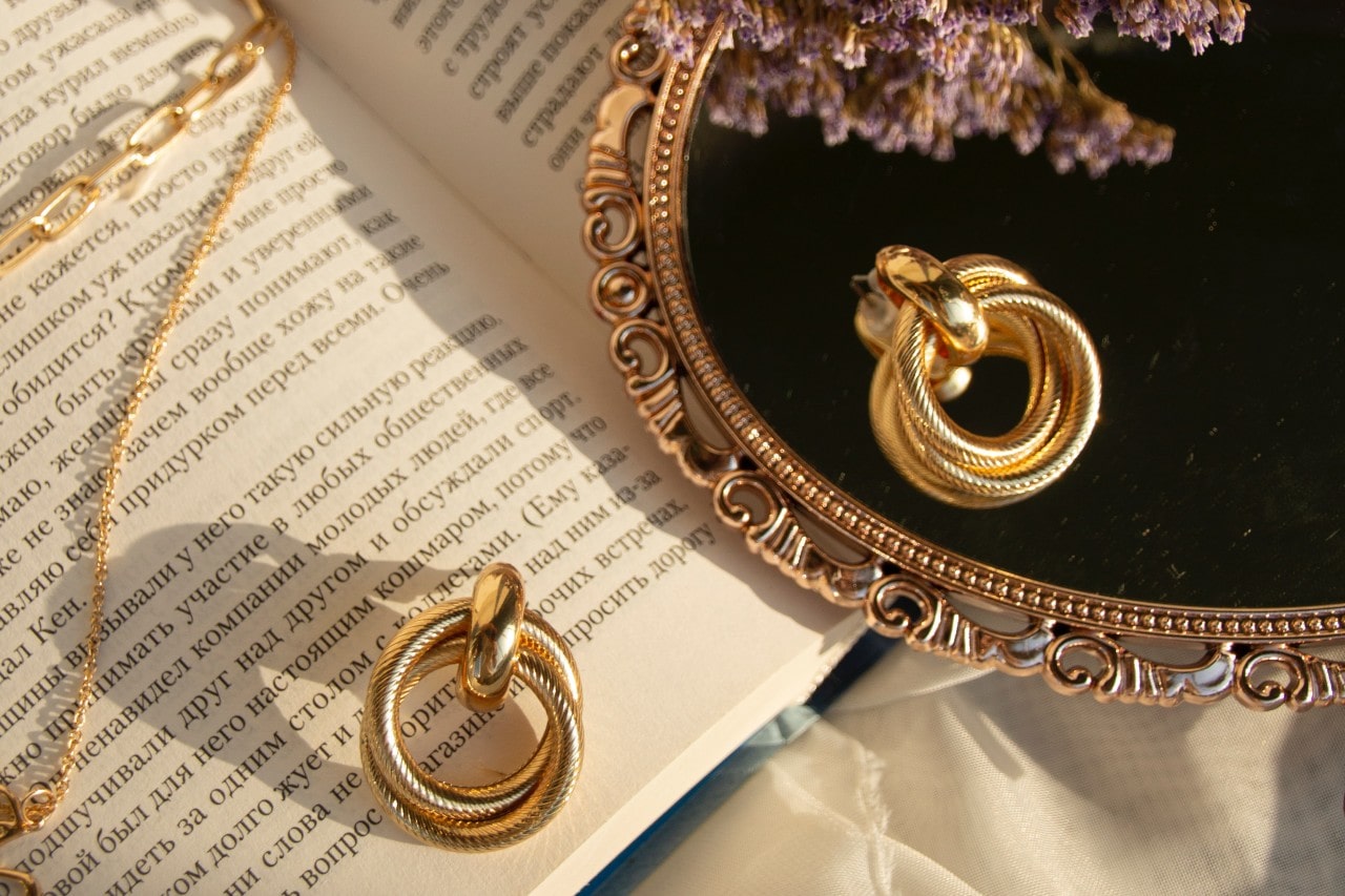 Pair of textured gold earrings lying on a mirror and a book