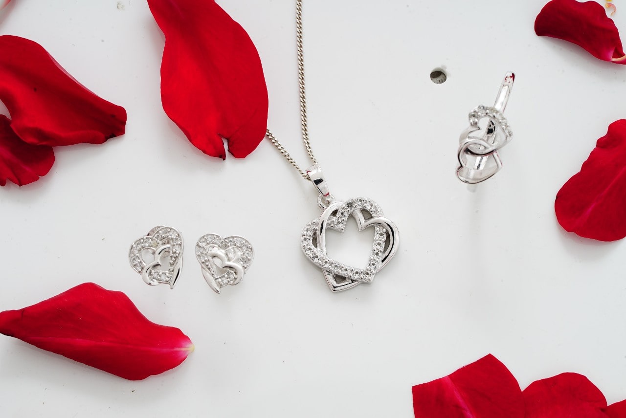 Set of silver heart jewelry set with diamonds with red rose petals lying around them