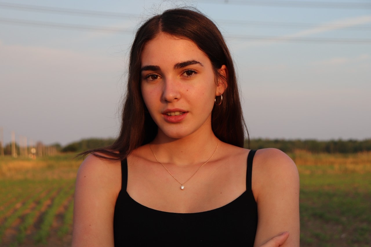 A woman wearing a simple solitaire necklace and hoop earrings stands in a flower field