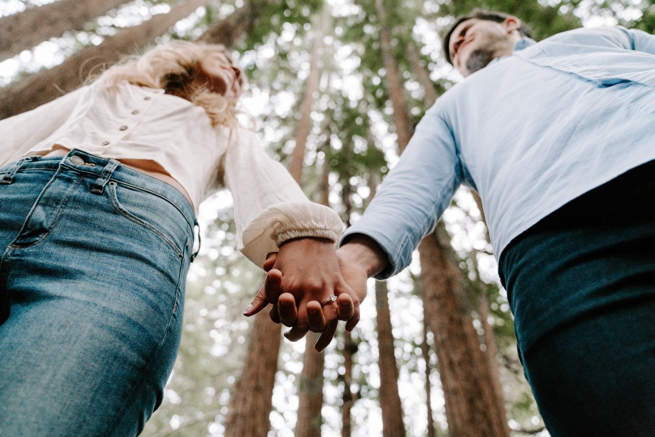 a couple holding hands in the forest, the woman wearing a diamond engagement ring