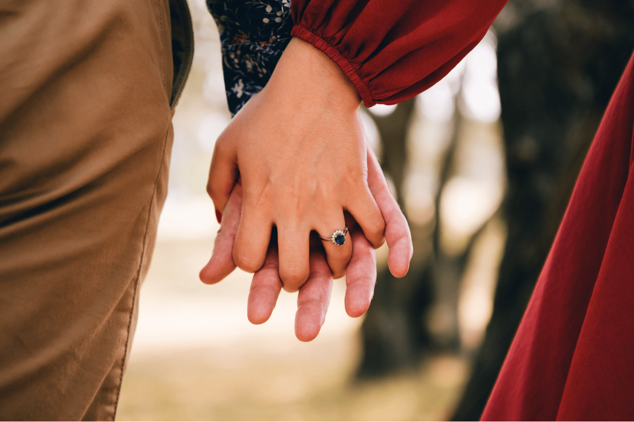 a couple holding hands, the woman wearing a sapphire engagement ring