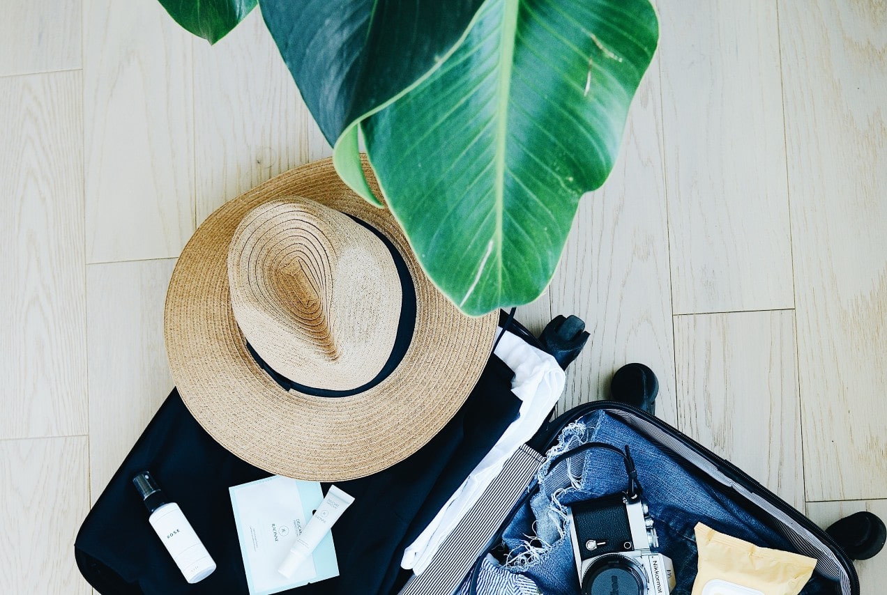 A suitcase full of clothes and accessories sits open on a floor by a plant.