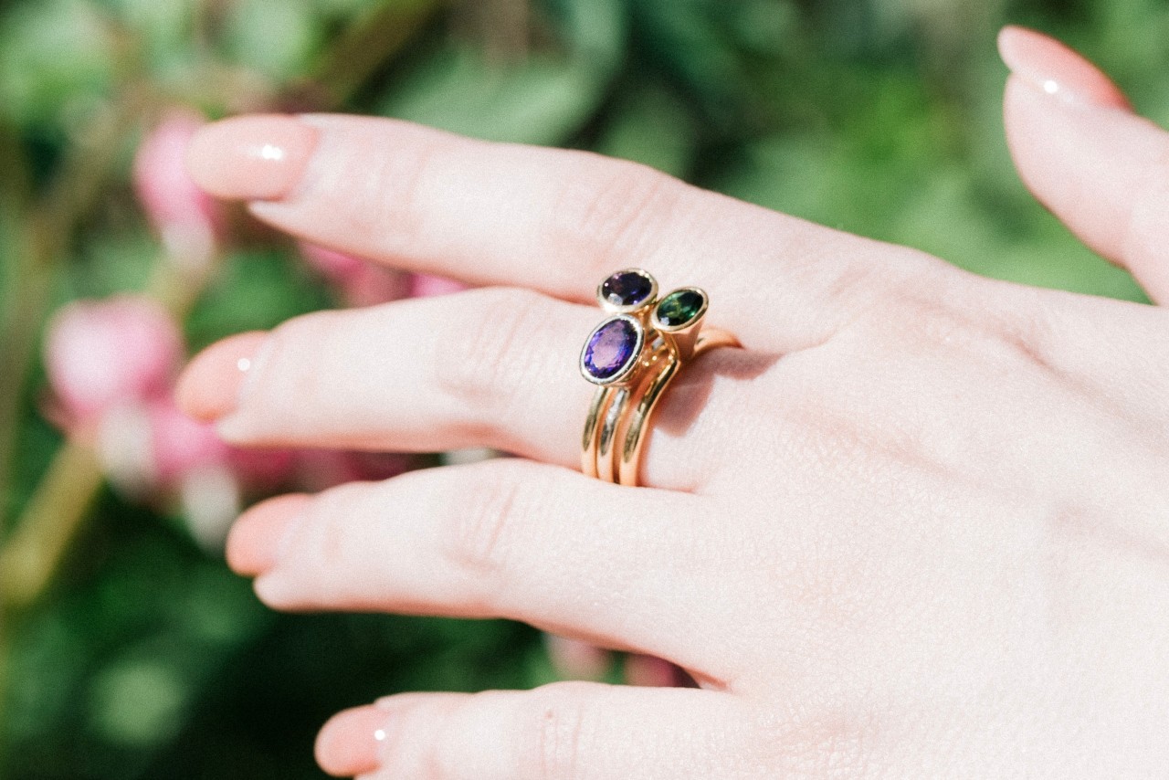 Three dark gemstone gold rings combined for a beautiful effect on a woman’s hand outside in front of flowers
