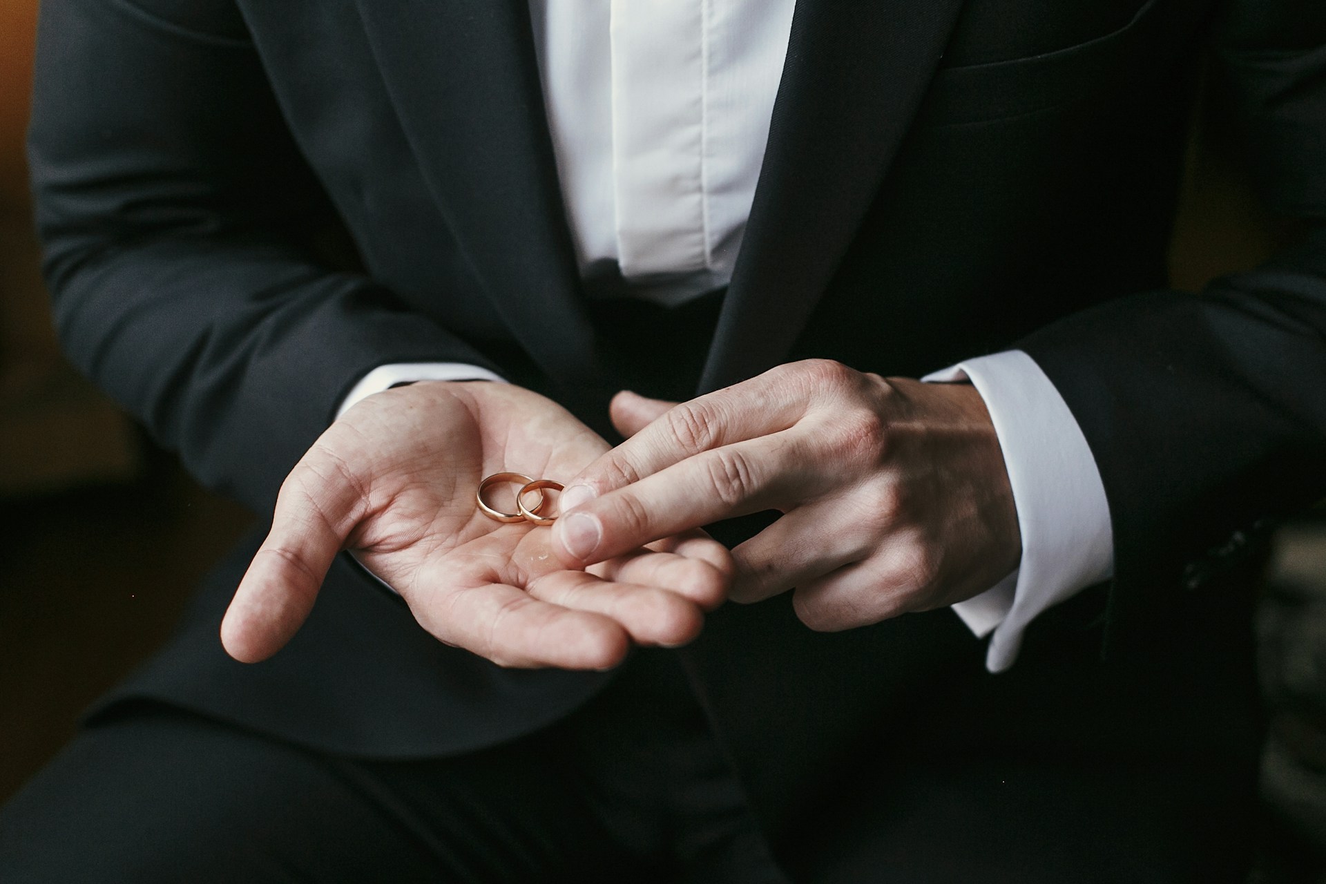 a groom’s hands holding two gold wedding bands