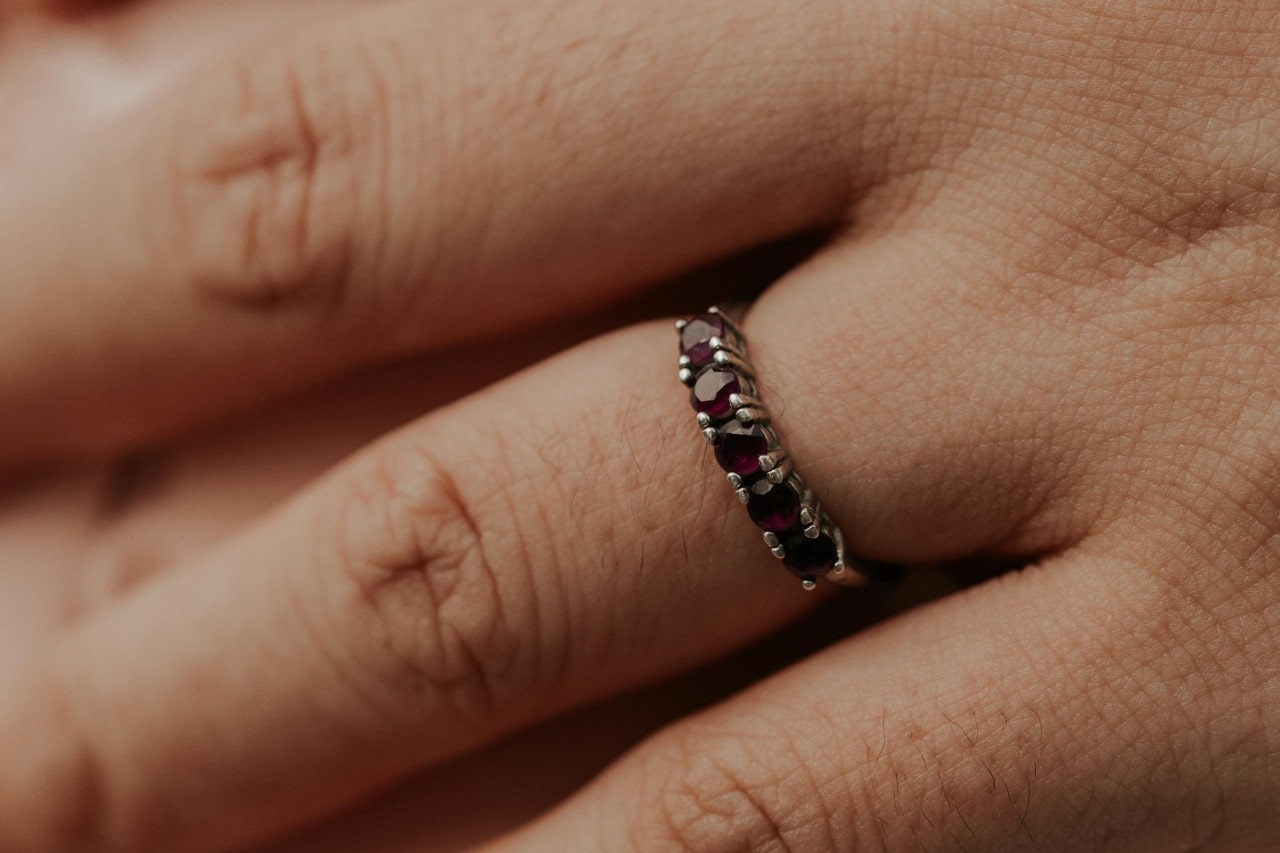 a close up image of a person’s hand wearing a ruby studded wedding band
