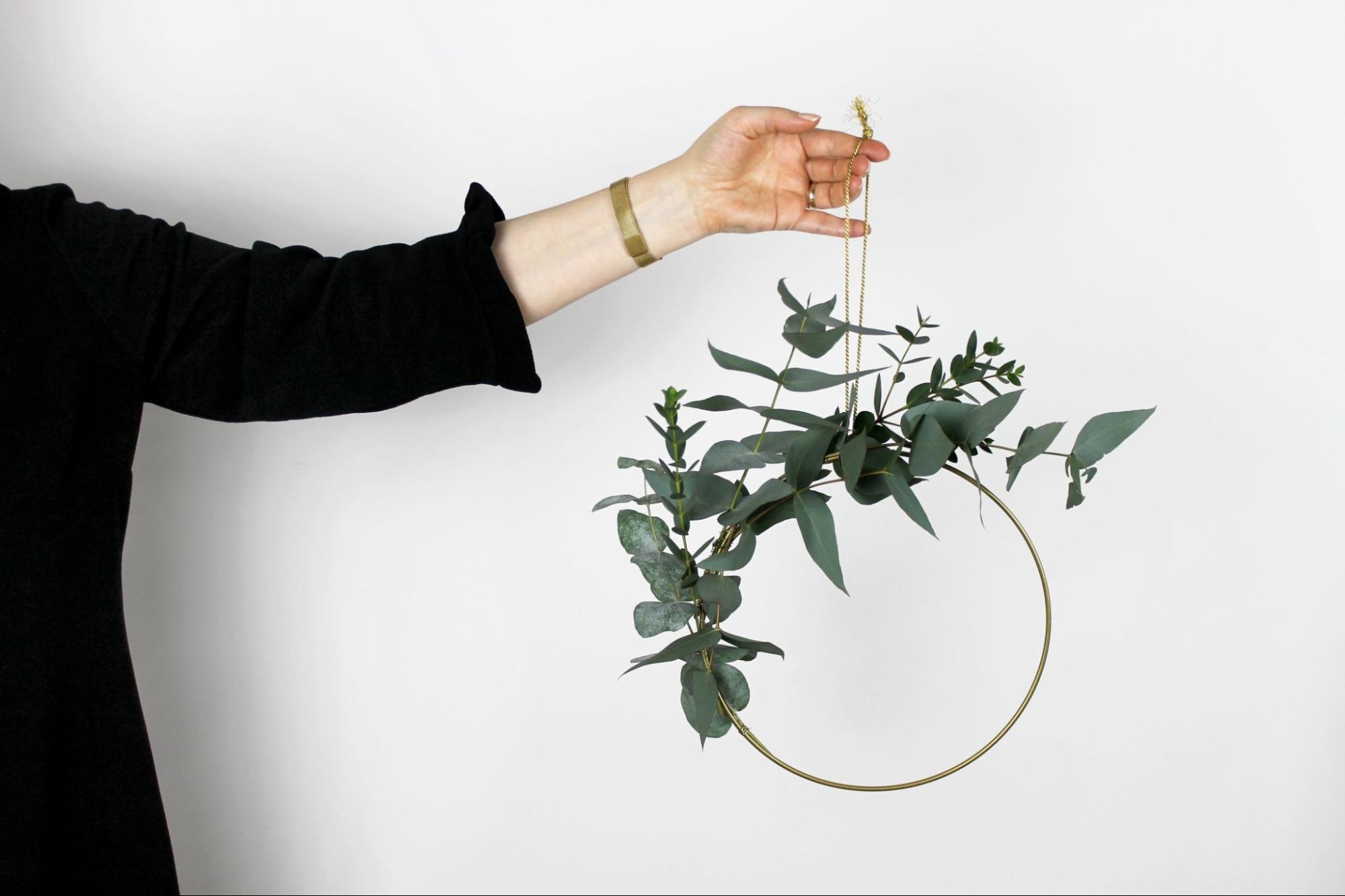 A woman’s outstretched arm holding up a wreath while wearing a gold bracelet.