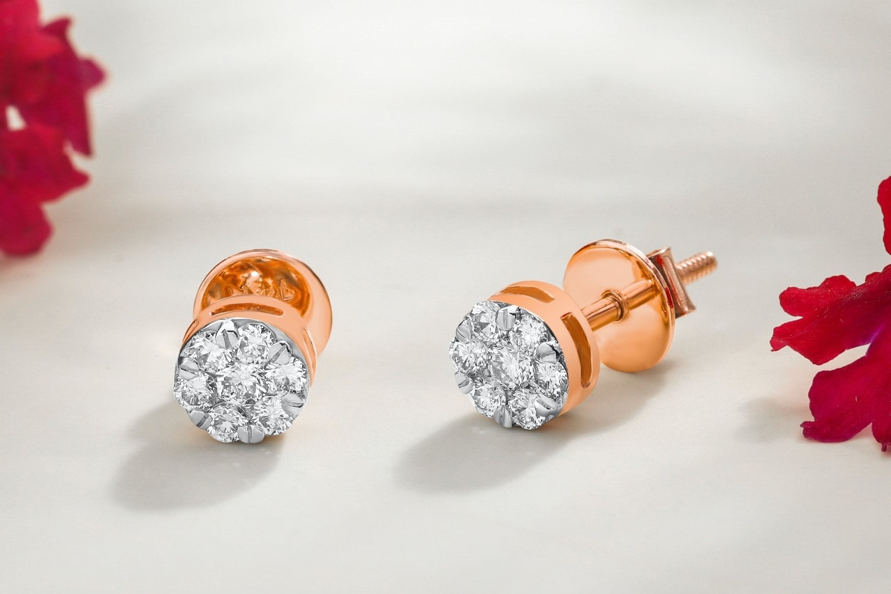 a pair of rose gold diamond stud earrings on a white surface next to red flowers