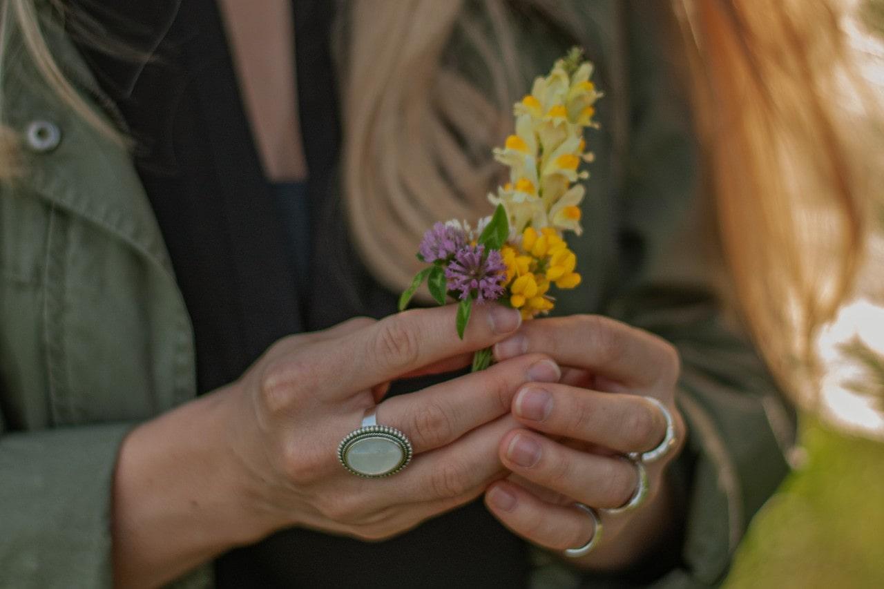 a woman holding purple and yellow flowers and wearing silver rings