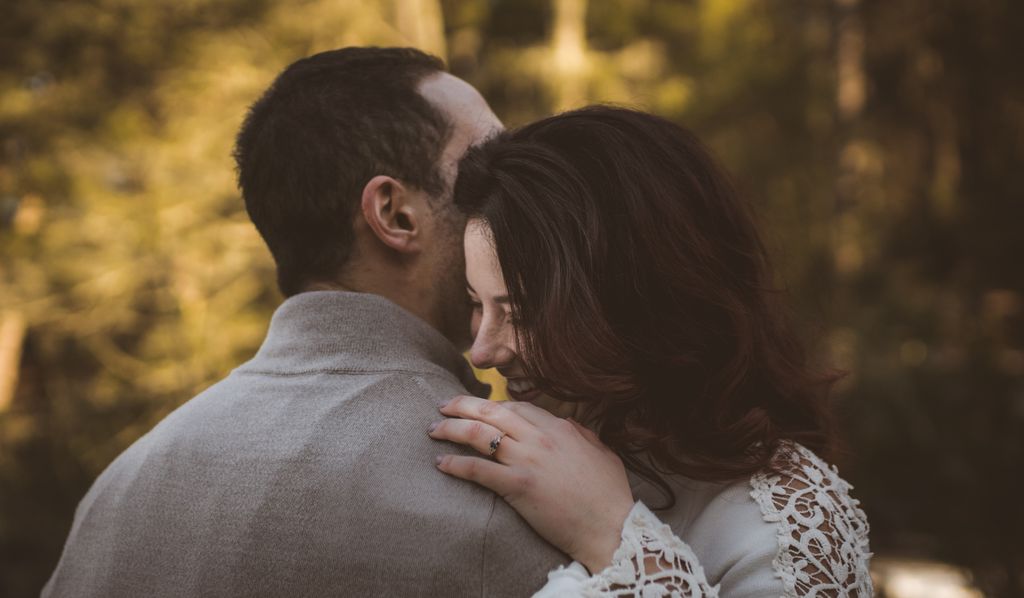 An engaged woman and her partner slow dance while outside.