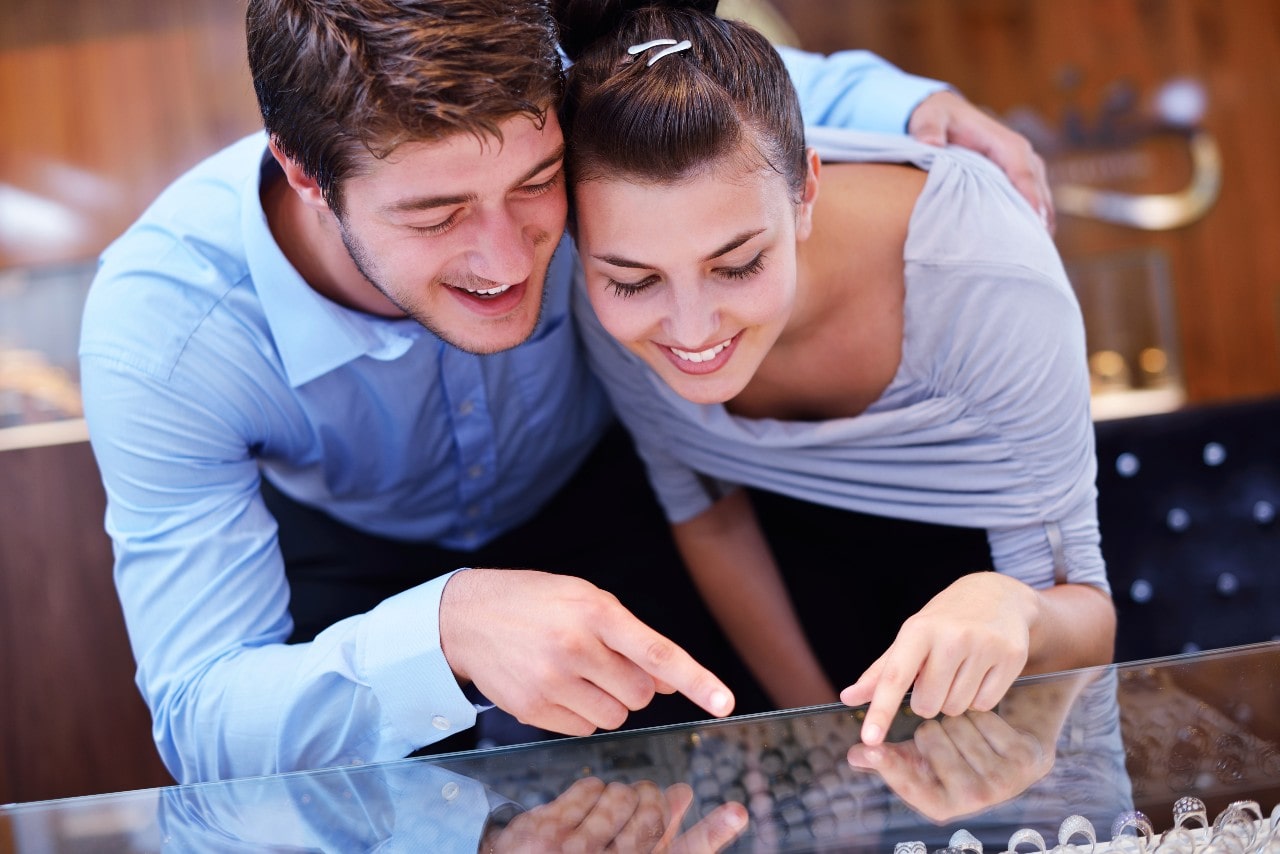 A couple in a jewelry store point and discuss different engagement ring styles.
