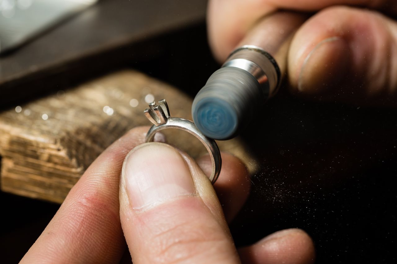 A jeweler is polishing a solitaire engagement ring setting with a tool.