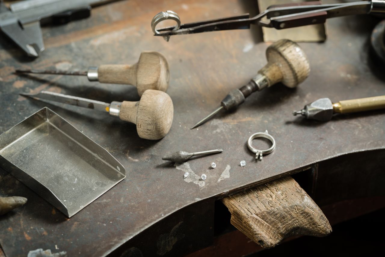 An engagement ring setting and four diamonds sit among tools at a jeweler’s workspace.