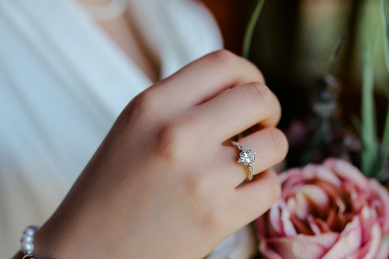 lady wearing a sparkling diamond engagement ring with a flower in the background