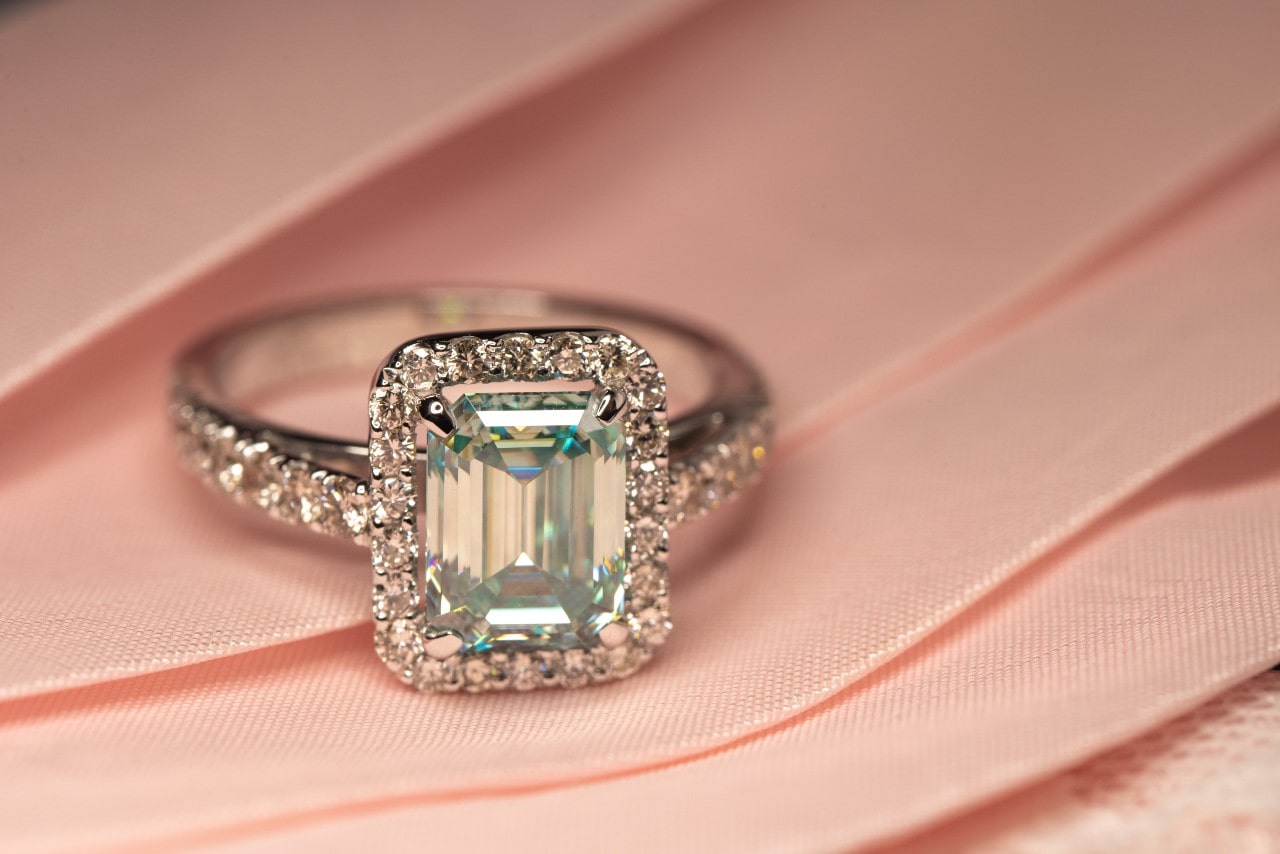 an emerald-cut halo engagement ring on a pink cloth