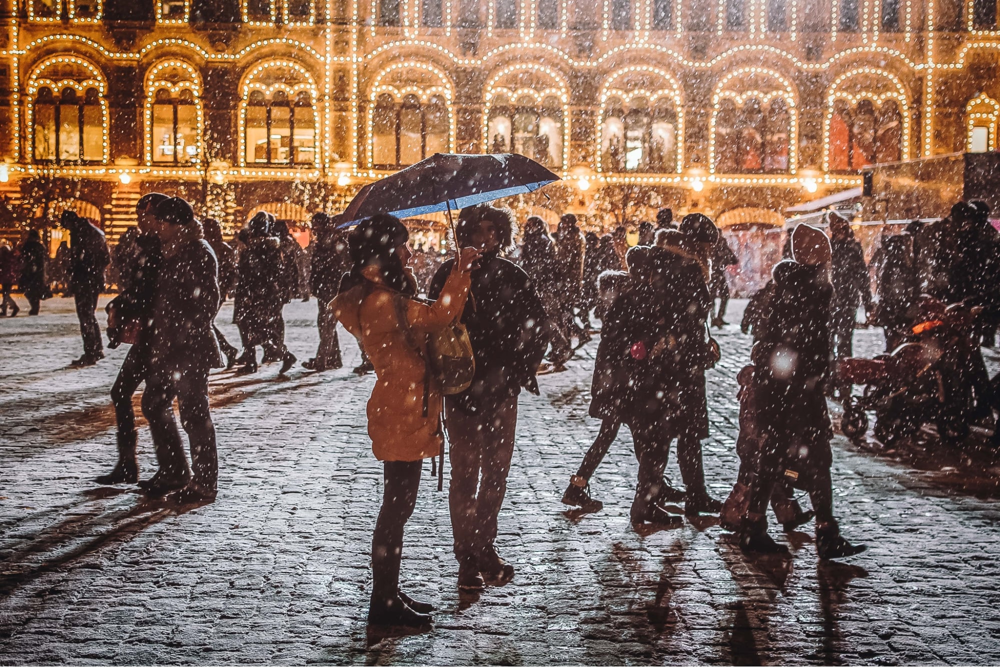 a couple standing under an umbrella during the holiday season