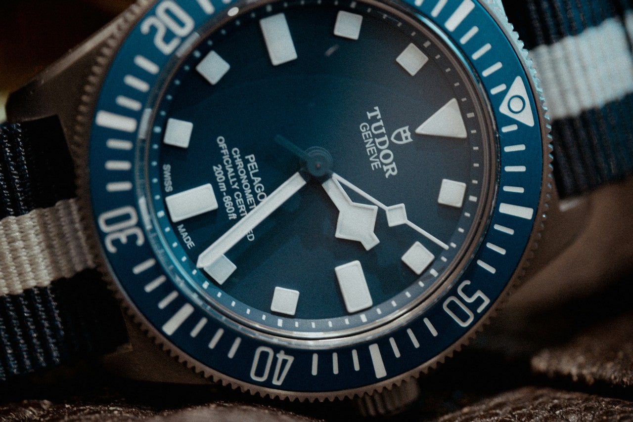 A close-up of a TUDOR Pelagos watch with a blue dial and rotating bezel, and a fabric strap.