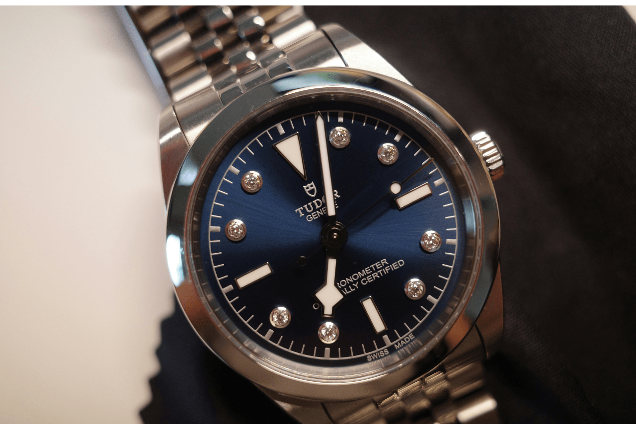 A close-up of a stainless steel TUDOR watch with a deep blue dial and diamond hour markers at 1, 2, 4, 5, 7, 8, 10, and 11.