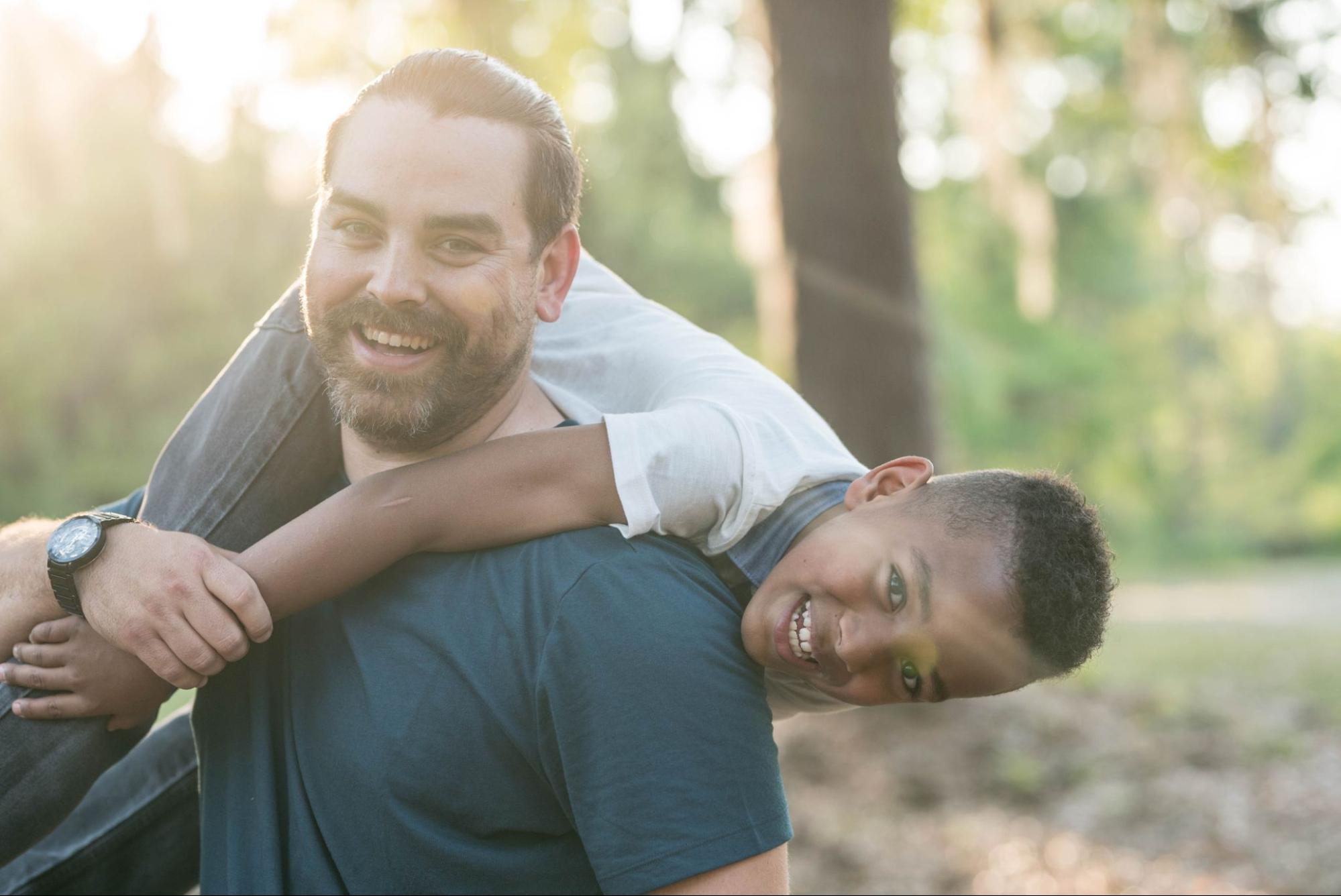 A picture of a dad wearing a sports watch holding his son over his shoulder, both smiling.