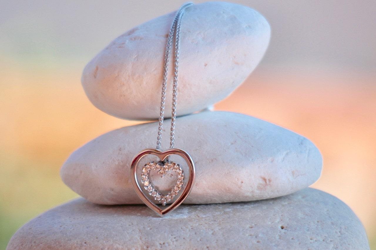 three stones piled on top of each other with a heart shaped pendant necklace lying over them