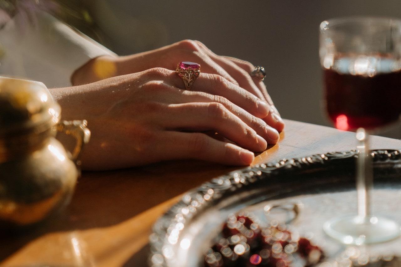 a woman’s hands resting on an extravagantly set table, wearing gemstone fashion rings
