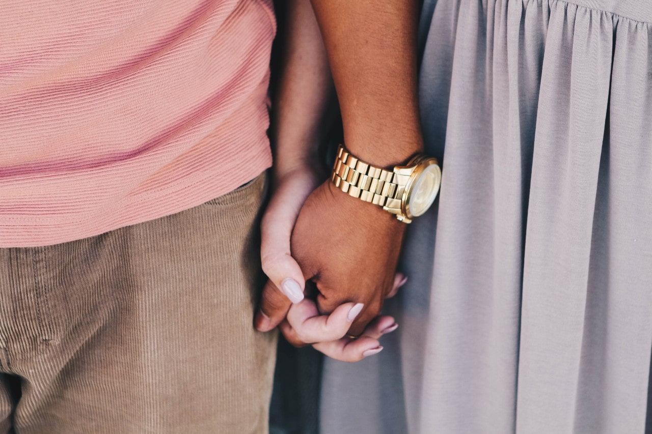 close up image of a couple holding hands, the man wearing a yellow gold watch
