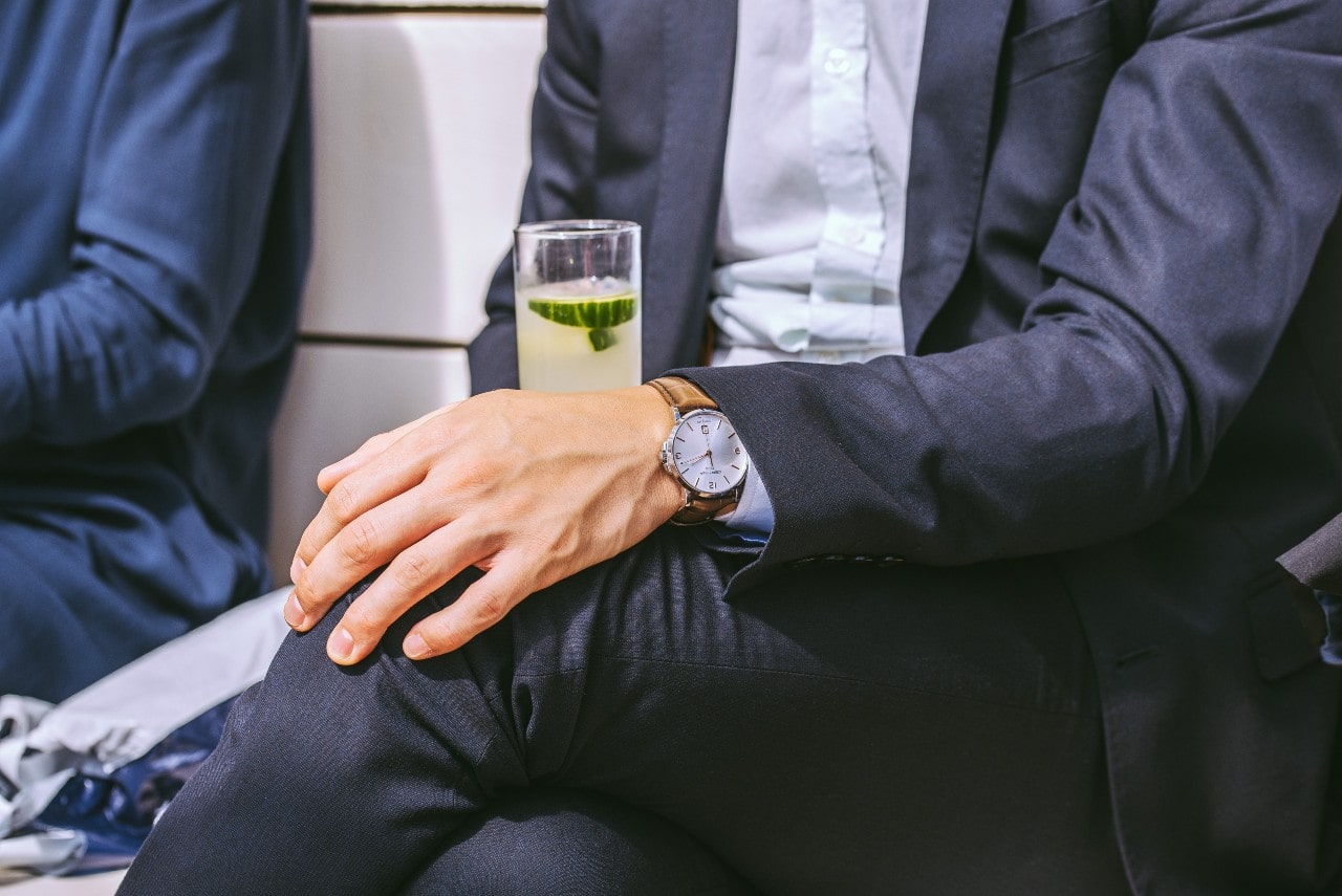 A businessman sits and waits in a lobby, sipping a limeade.