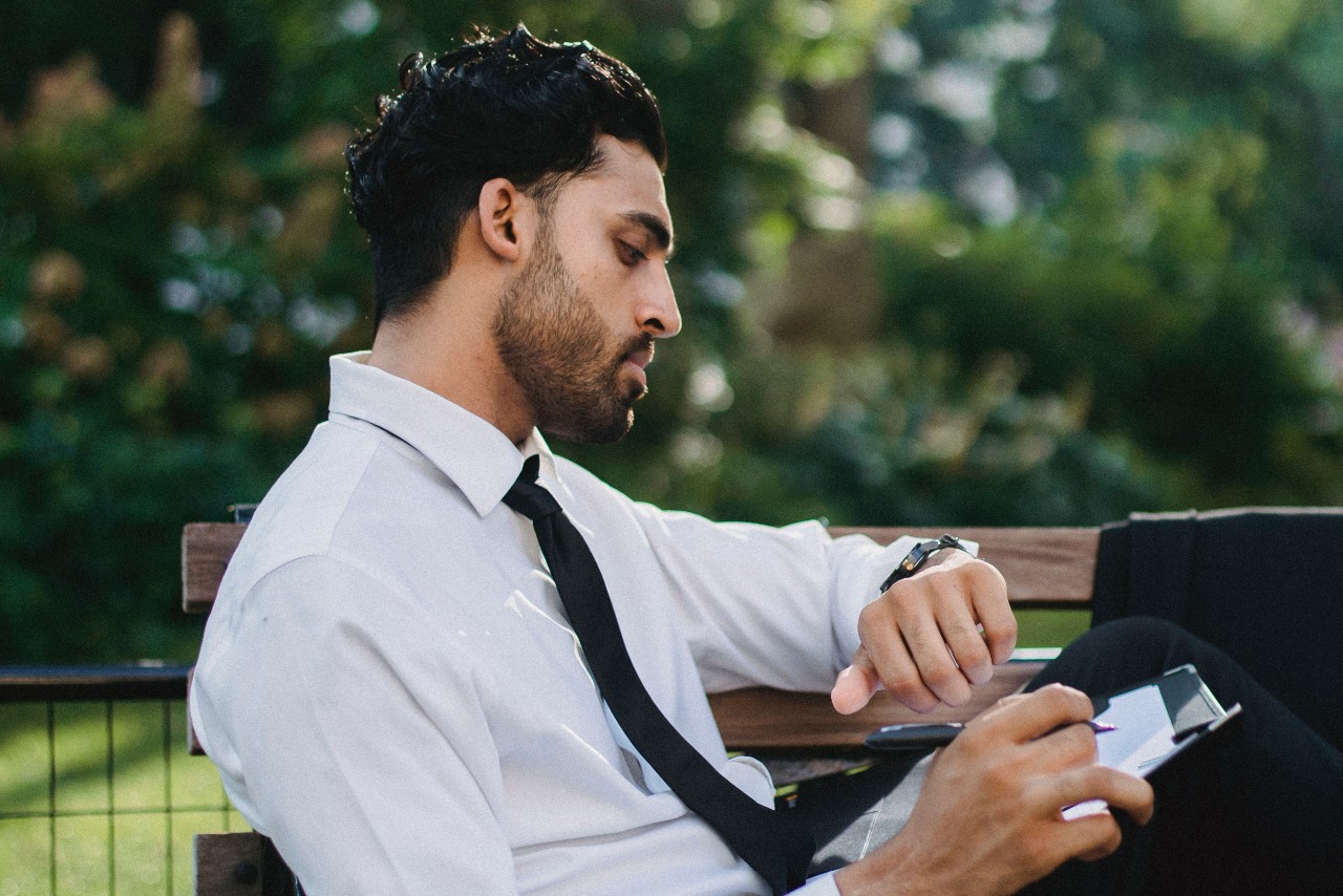 A businessman checks his watch as he works on a proposal on a park bench.