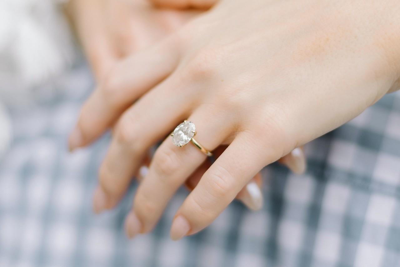 a woman’s hands crossed in front of her, adorned by a solitaire, oval cut engagement ring