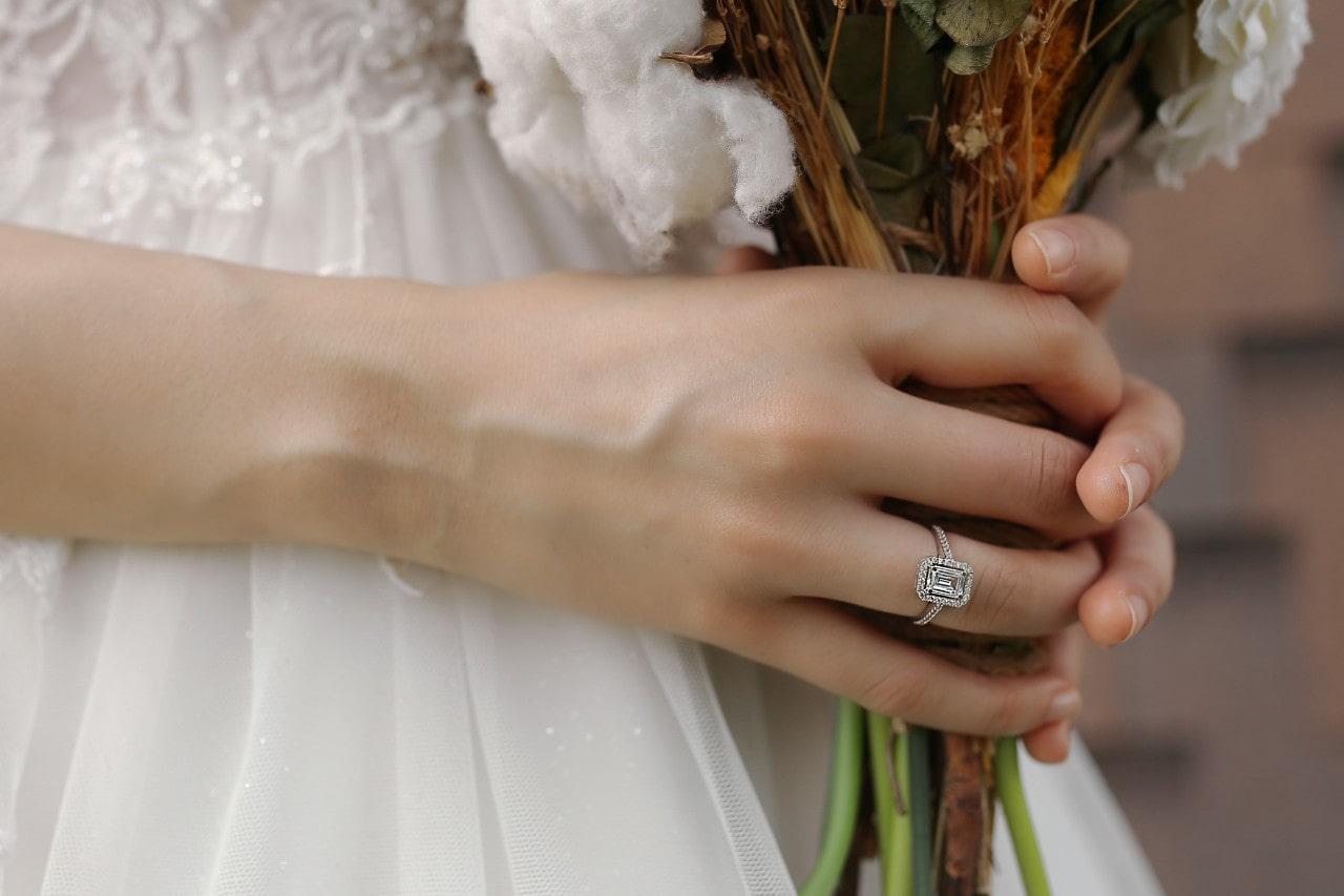 a bride holding her bouquet and wearing a halo emerald cut engagement ring