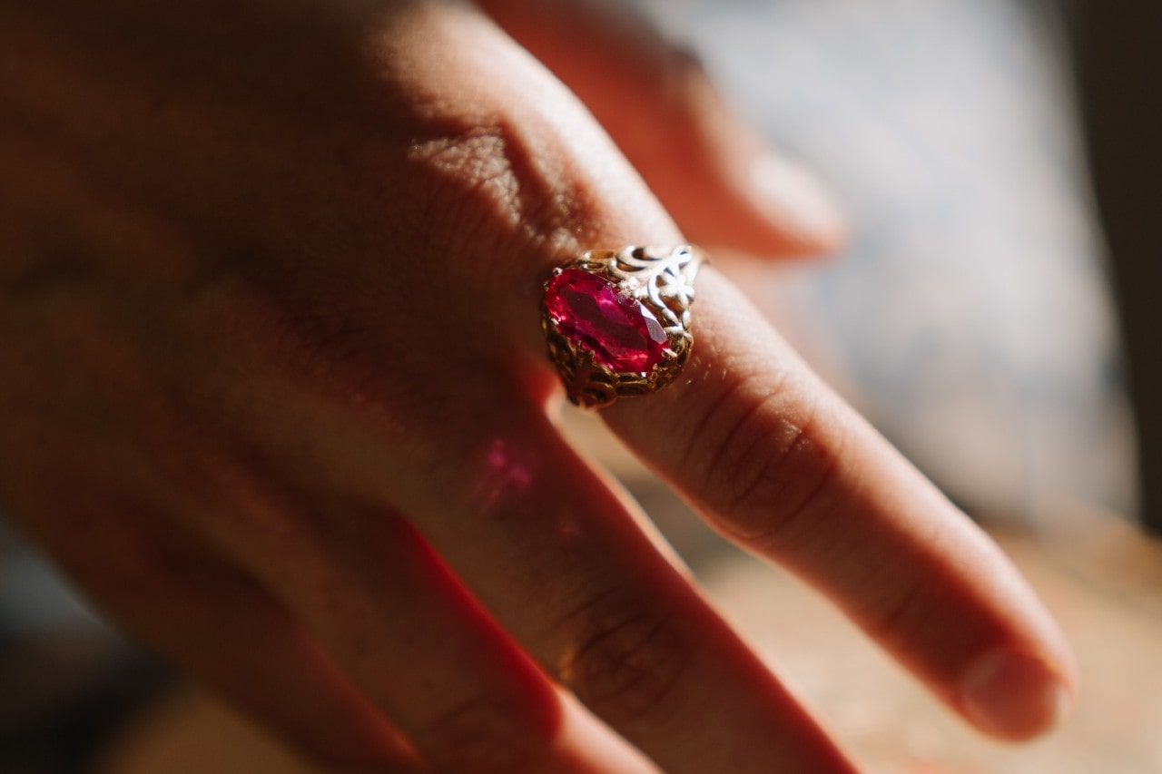 close up image of a hand wearing a bold statement ring featuring a pink gem