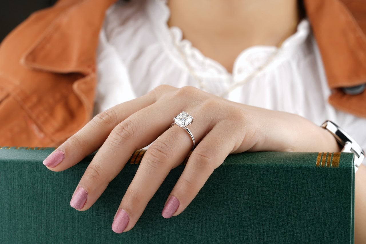 A white gold oval cut ring on a woman’s hand as she holds a green book.