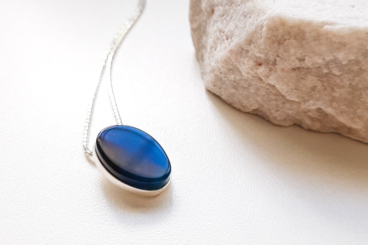 a white gold pendant necklace featuring a deep blue gemstone next to a white rock