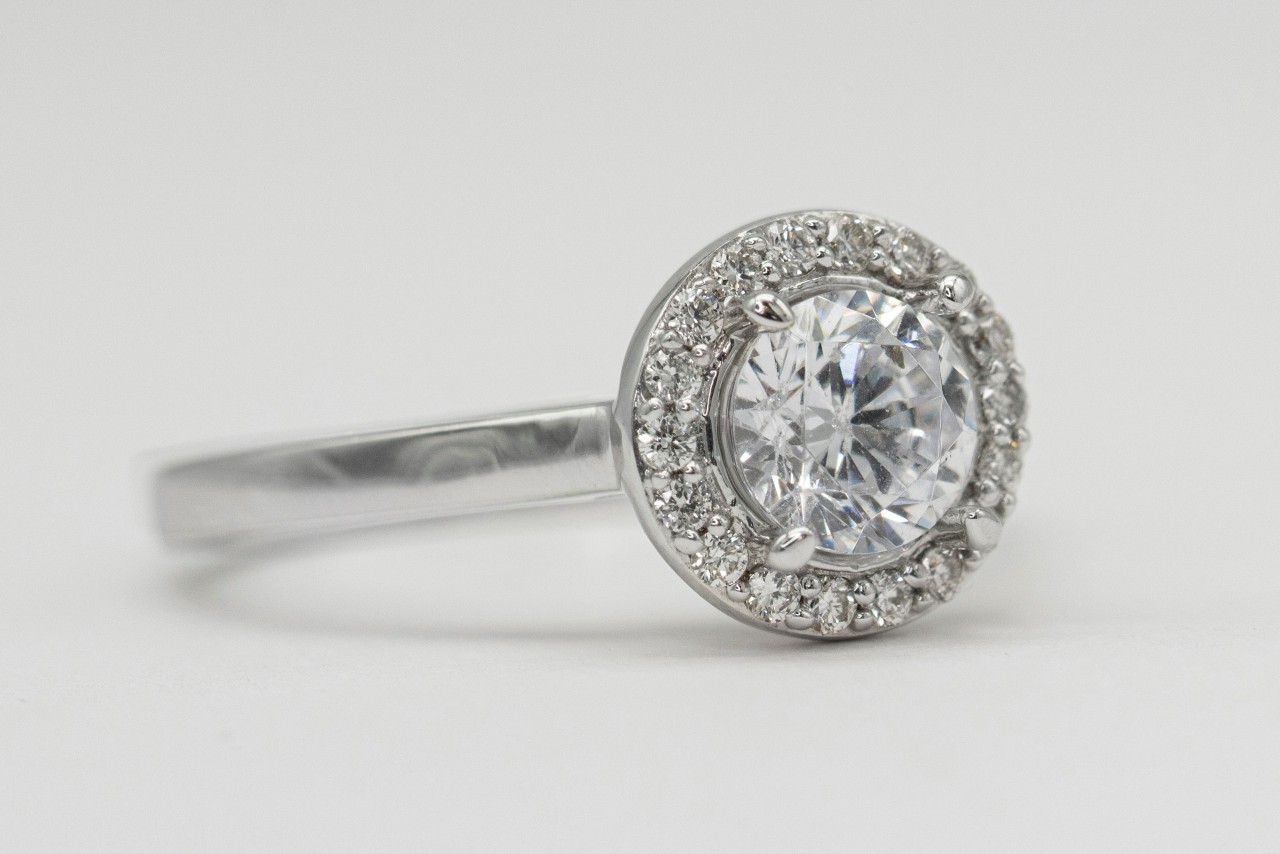 A close-up of a diamond halo engagement ring with a round center stone set in a white gold band. A close-up of a diamond halo engagement ring with a round center stone set in a white gold band.