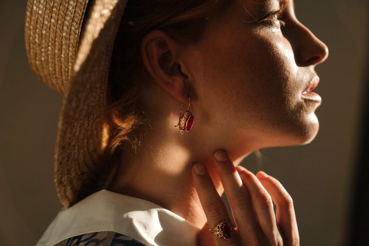 A woman looking into the light touches her neck while wearing jewelry.