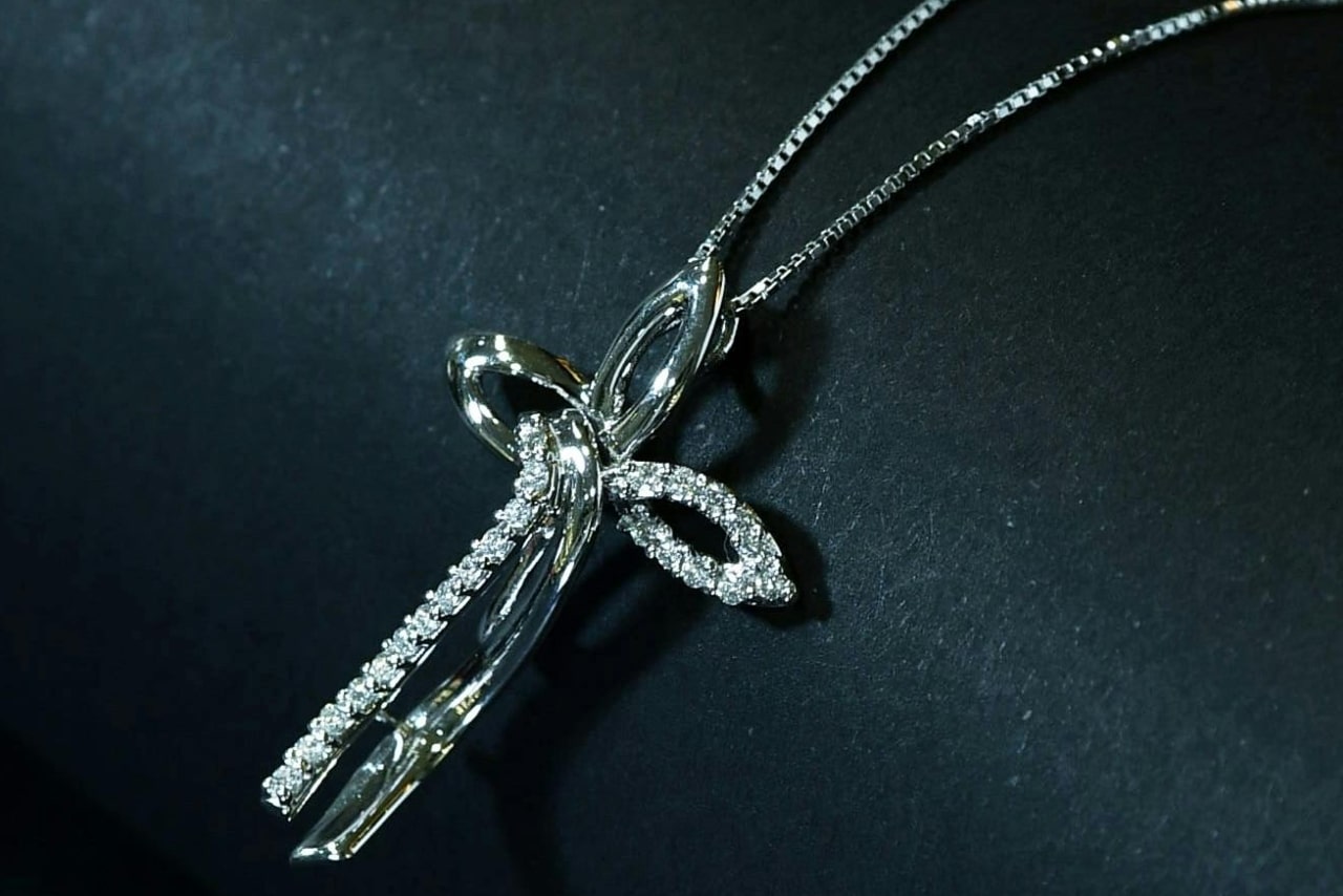 A silver cross-shaped pendant adorned with sparkling diamonds, set against a dark background. A silver cross-shaped pendant adorned with sparkling diamonds, set against a dark background.