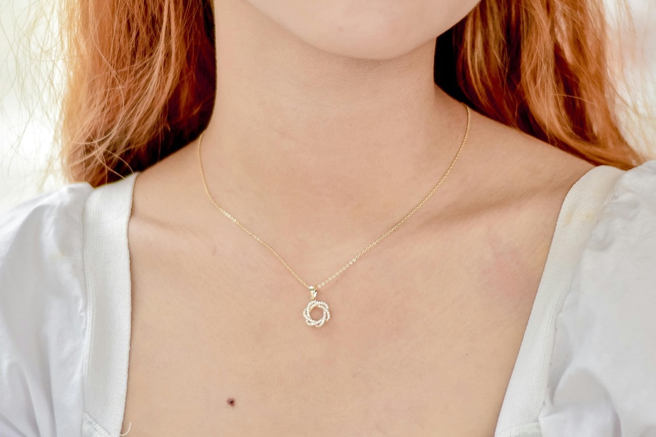 A young woman wearing a gold necklace with a small, intricate circular pendant, complementing her light skin and red hair. A young woman wearing a gold necklace with a small, intricate circular pendant, complementing her light skin and red hair.