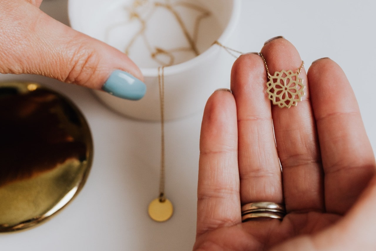 A close-up of a woman’s hands as she selects a gold necklace from her collection. A close-up of a woman’s hands as she selects a gold necklace from her collection.