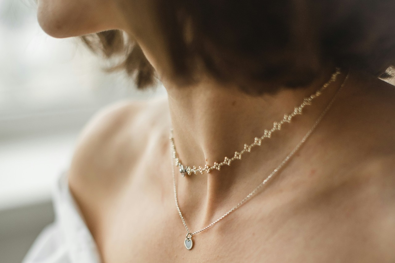 A close-up of a woman’s neck and shoulders adorned in two delicate gold necklaces. A close-up of a woman’s neck and shoulders adorned in two delicate gold necklaces.