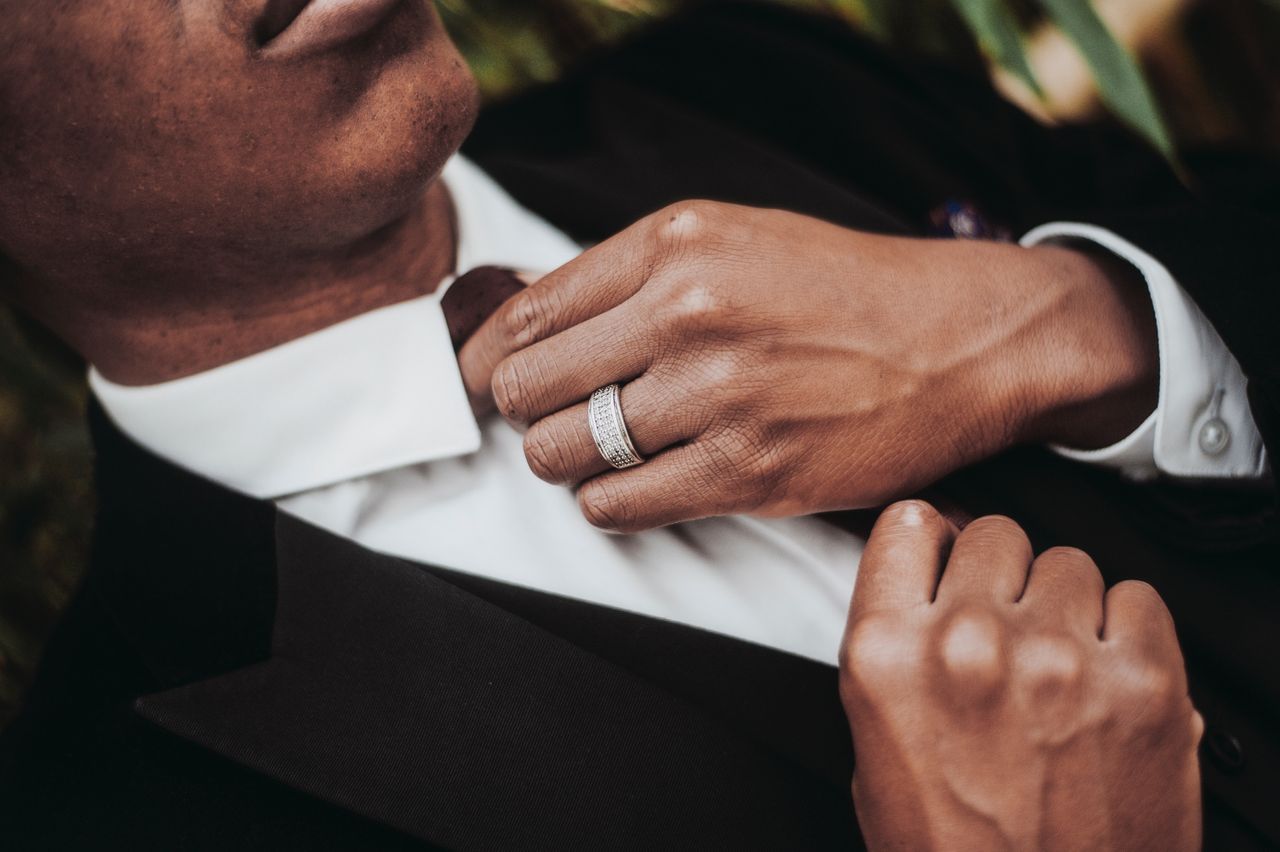 A closeup of a man adjusting his tie and wearing a diamond-studded silver wedding band