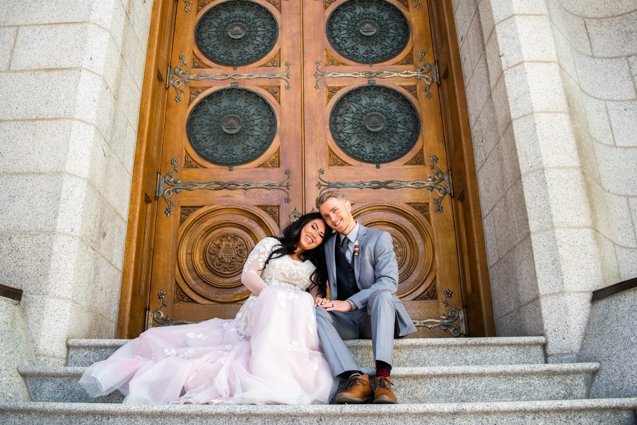 A newlywed couple sits on the stairs outside their chapel.