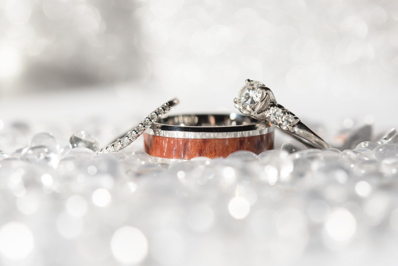 A woman’s pave diamond wedding band leans on top of a man’s wedding man with a diamond engagement ring.