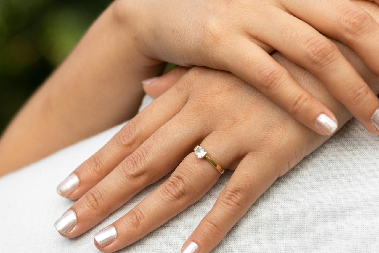 a woman’s hands on a person’s back, adorned by a solitaire engagement ring with gold band a woman’s hands on a person’s back, adorned by a solitaire engagement ring with gold band